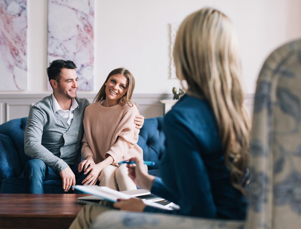 A happy couple sitting close together on a couch, smiling and reconnecting during a couples therapy session with a licensed therapist in Las Vegas, NV, demonstrating the trust and intimacy rebuilt through EFT couples counseling with Dr. Belle, PhD, LMFT.