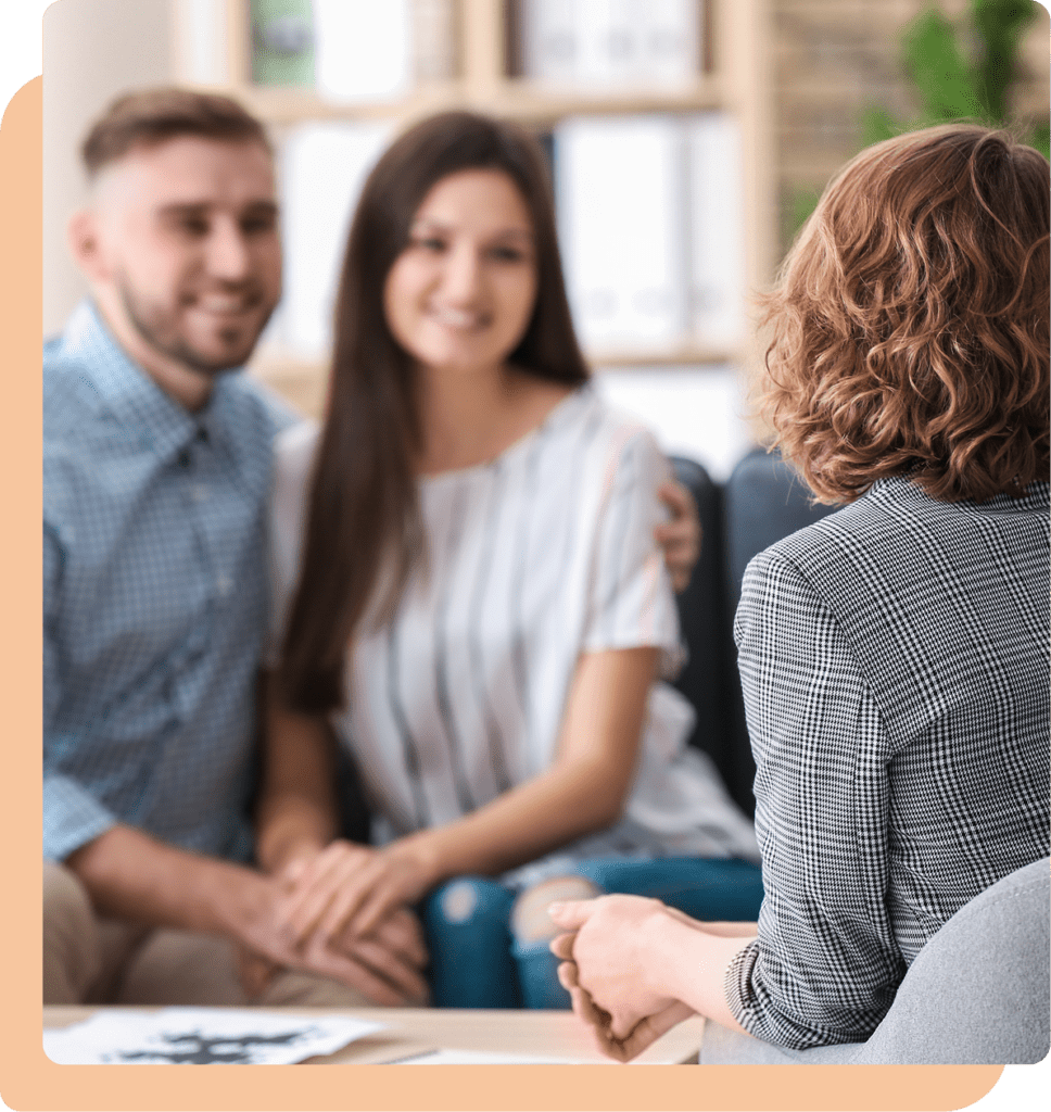 A smiling couple holding hands while meeting with a therapist.