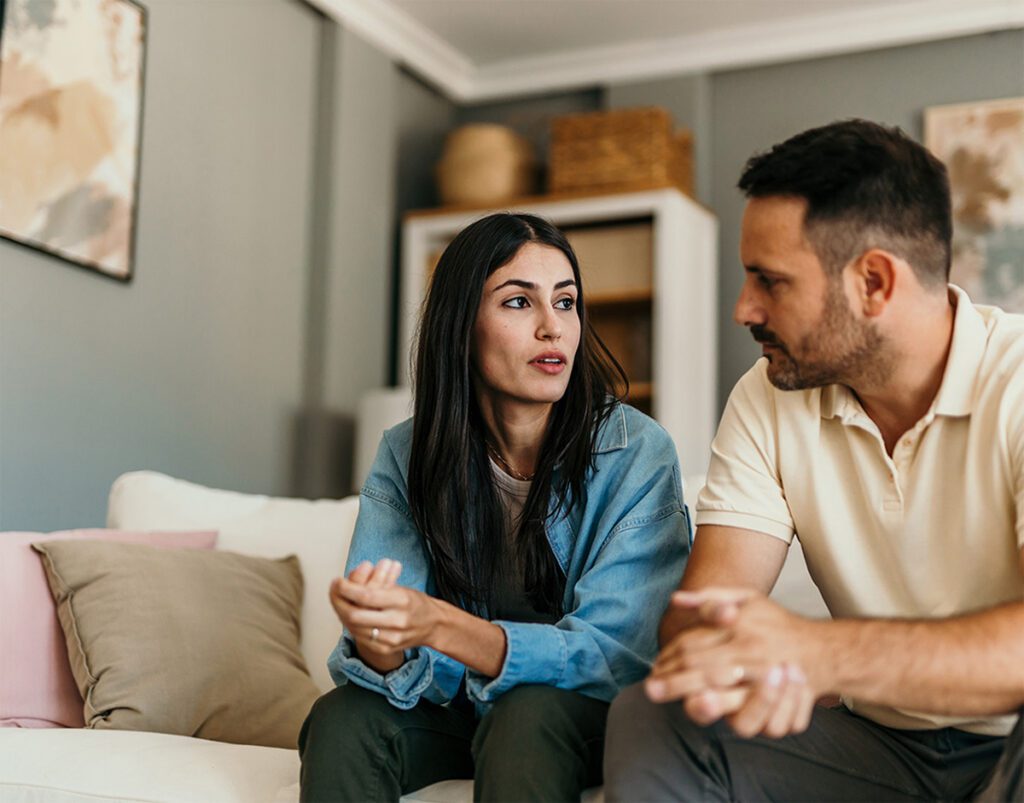A couple sitting on a couch having a conversation in a therapy session.