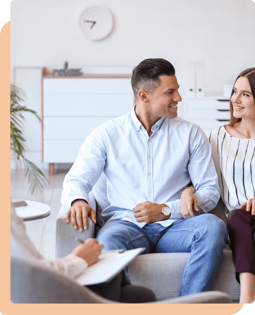 A smiling couple sitting together on a couch during a couples therapy session.