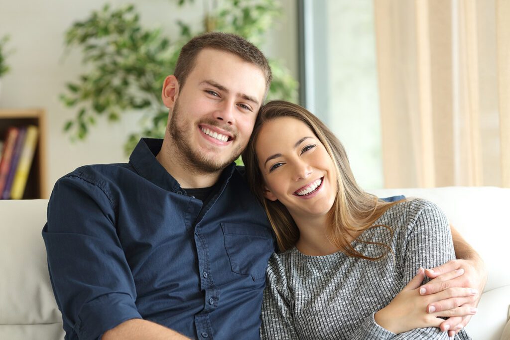 A happy couple smiling and cuddling on a couch, representing the reconnection and relationship growth achieved through couples therapy in Las Vegas with Dr. Belle, LMFT