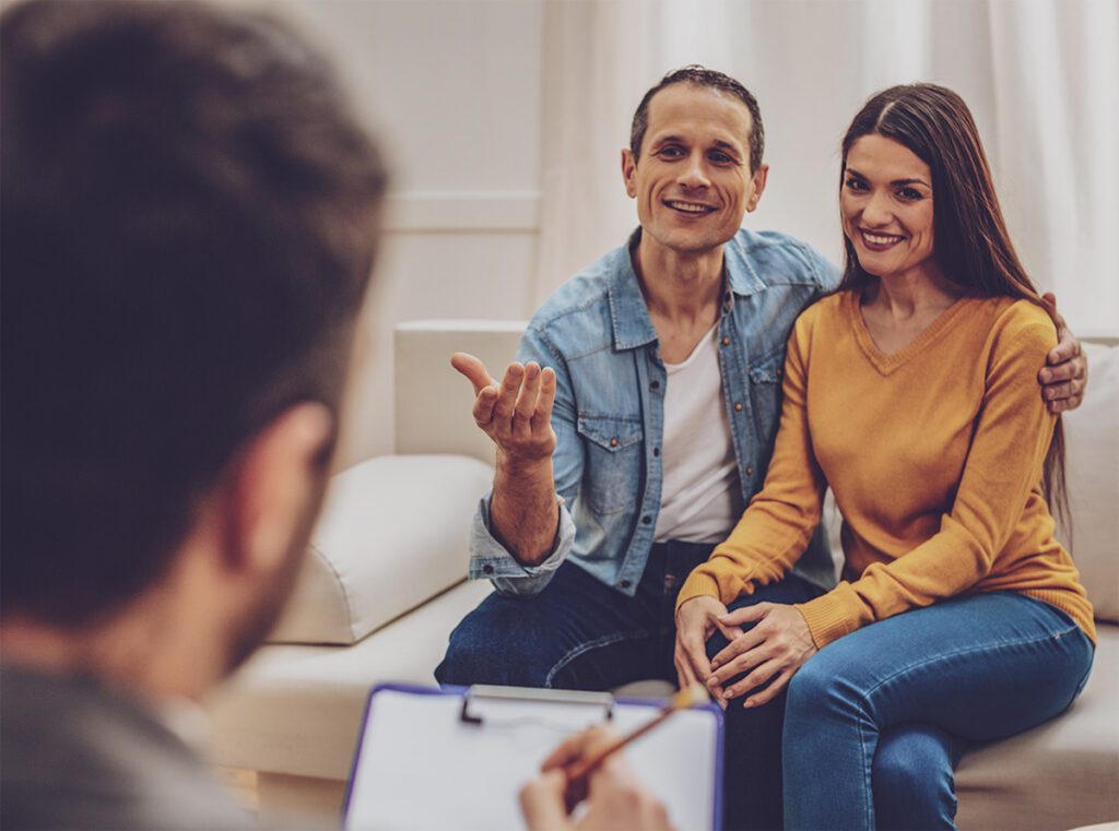 A couple sitting closely together on a couch communicating with a therapist.