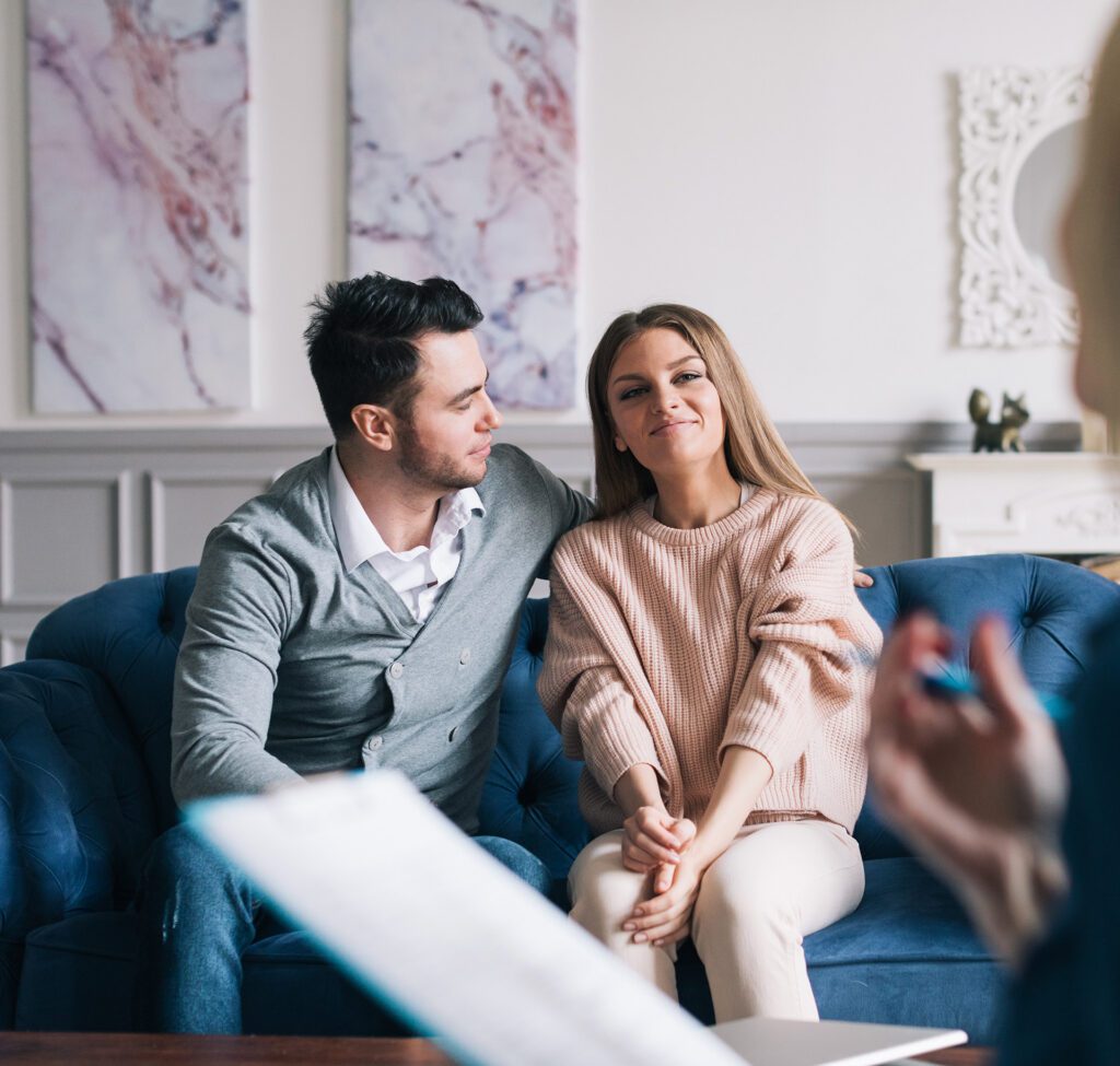 A young couple sitting close together, holding hands and smiling during a faith-based Christian marriage counseling session in Las Vegas with Dr. Belle, LMFT